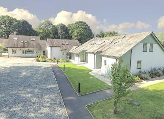 A chalet bungalow in Windermere overlooks a front lawn and a large parking area.