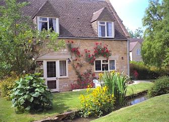 A modern brick cottage overlooking a lawn with s small millstream running through it.