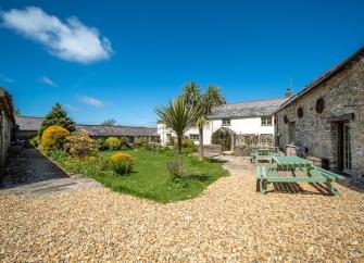 A large Devon farmhouse overlooks a lawn and drive with a picnic table.