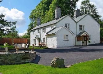 A large twin-gabled house overlooks a lawn with a water-feature.