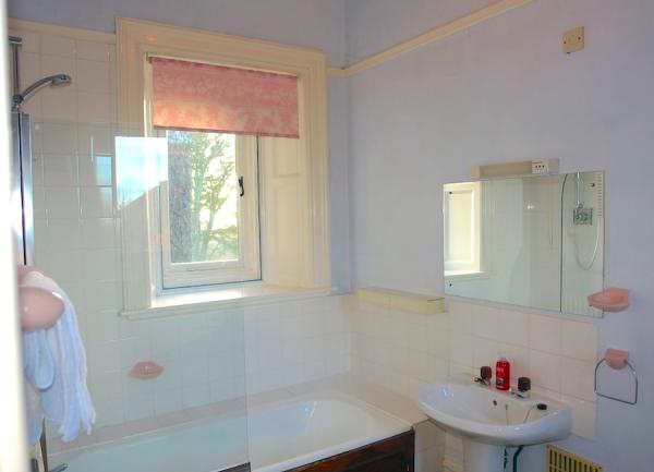 A bathroom with a bath with an overhead shower and washbasin.