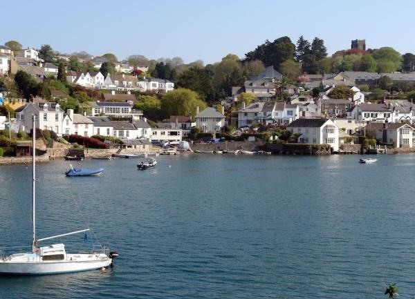 A cluster of houses overlook an estuary at high tide with yachts and other small craft moored to a quay.