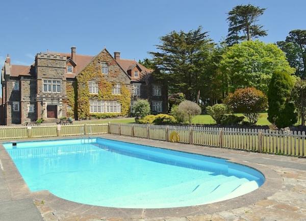 A large country house overlooks gardens with an outdoor swimming pool.