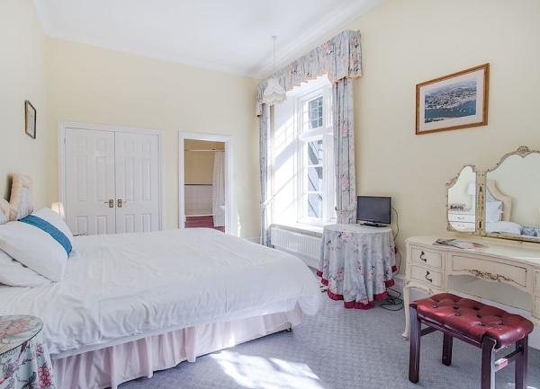 Double bedroom with large windows containing a bed, dressing table, side table and TV.