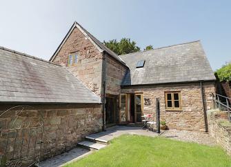 A stone-built holiday barn conversion overlooks a large lawn.