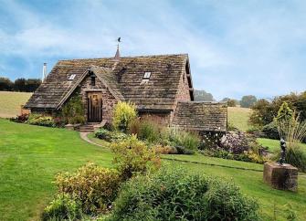 Exterior of a coach house conversion surrounded by a large garden with shrubs.