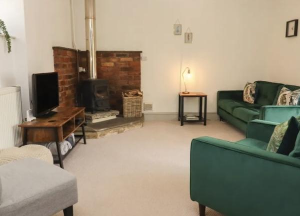 A 3-piece suite and additional chair face a TV on a table and a hearth with a wood burner in a lounge.