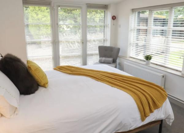 A twin aspect double bedroom with venetian blinds and and a bedside chair.