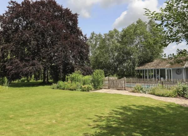 A large, fenced lawn with flower-filled borders and a copper beach tree in the far corner.