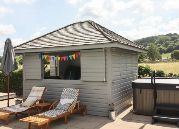 A patio with a hot tub shelter, sun loungers and a BBQ