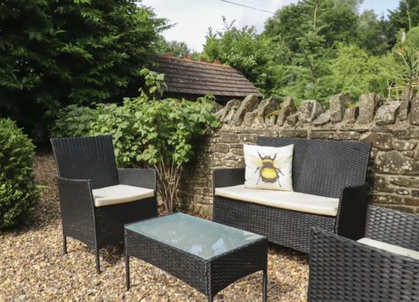 A garden corner by a stone wall, aset of wicker chairs seating 4 face around a coffee table