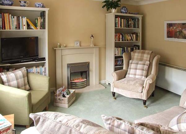 A lounge with a sofa and armchaircentred around anopen fireplace and a TV on a tall set of bookshelves.