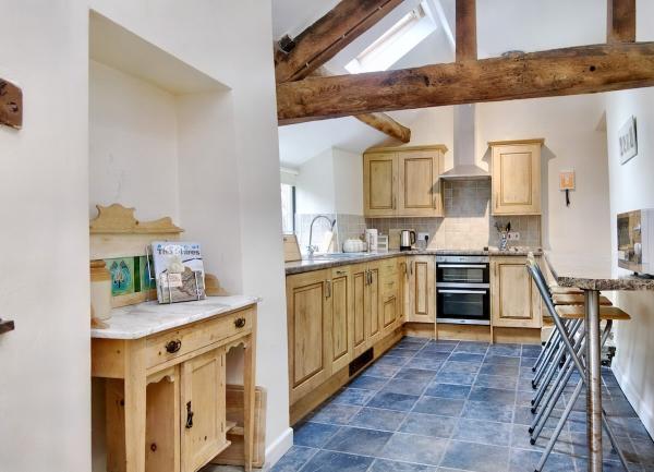 A kitchen with oak beams, tiled floor, fitted units and a breakfast 'table-shelf' with stools on one wall.