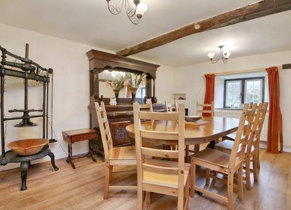 A dining room with a wooden dining table and 8 chairs. An antique apple-press stands in one corner.