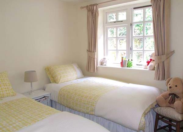 A twin bedroom with  a bedside cabinet with a table light and a teddy bear perched on a bedside chair.