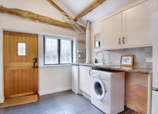 A tiled utility room with a washing machine, sink, cupboards and worktops.