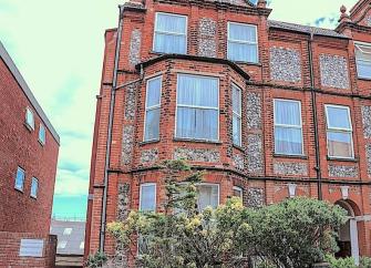 Exterior of a brick-built, 3-storey seaside townhouse with a small front garden.