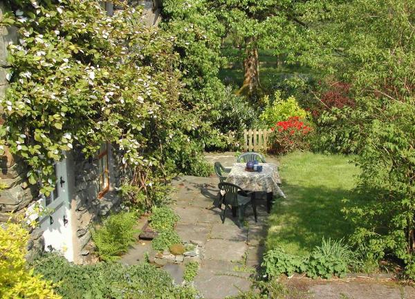 Garden patio with table and chairs surrounded by a lawn and mature trees.