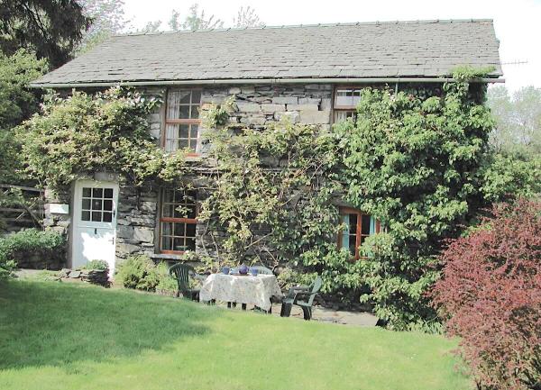 A vine-clad stone cottage overlooks a patio and lawn.