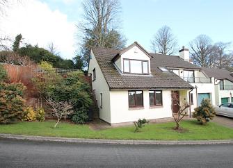 A modern 2-storey Exmoor house with a glass-fronted balcony and a lawn dotted with small trees