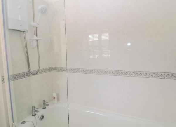 Tiled bathroom with a bath with n overhead shower.a