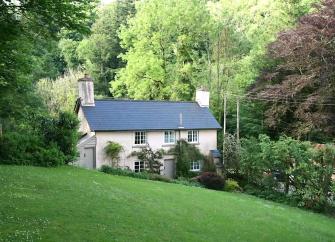 Double-fronted cottage with large lawn surrounded by mature trees.