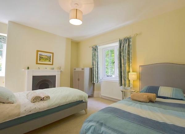 Twin bedroom with beds, bedside lights, cupboard and fireplace.