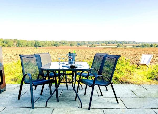 Dining table and chairs on a patio with views across open fields.