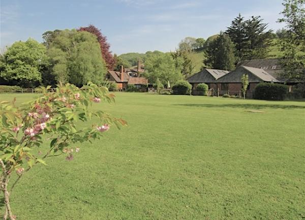 A playing field overlooked by a cluster of barn cottages.