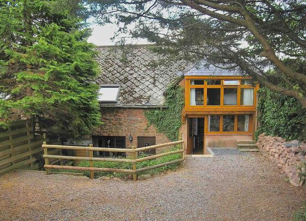 Exterior of a 2-storey barn conversion partly shaded by trees.