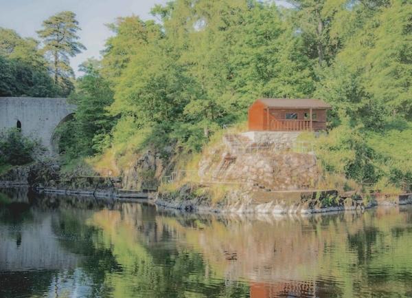 Trees and a lodge reflected in the calm water of a river.