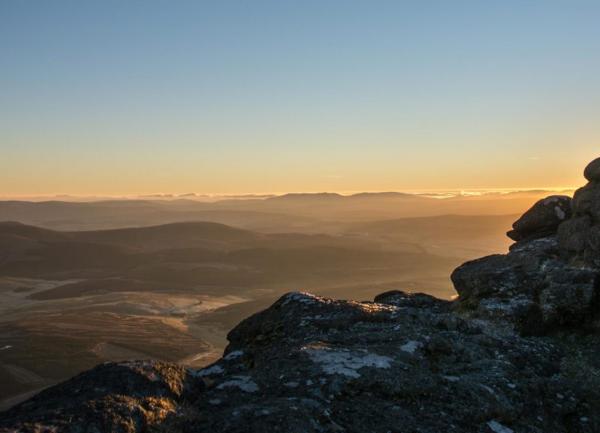 Mountain top view of crags silhouetted in the setting sun.