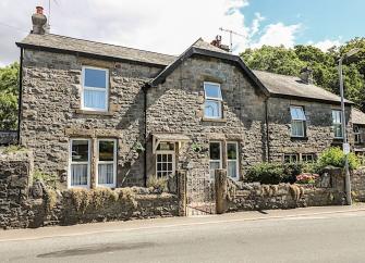 Stone-built Cumbrian holiday cottage with a front garden behind a low stone wall.