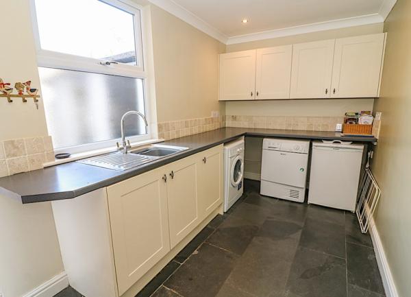 Utility room with sink, washing machine and cupboards.