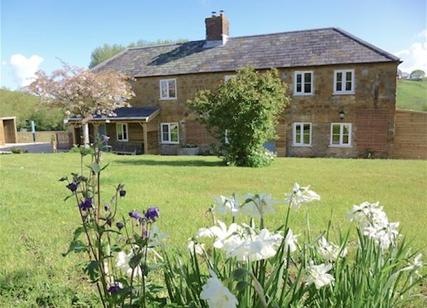 Front exterior of a long farmhouse overlooking a spacious lawn.