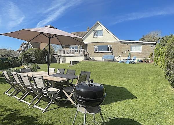 Table, chairs, parasol and BBQ on a lawn.