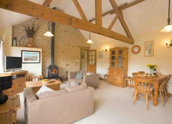 A spacious, oak-beamed lounge area with sofas, TV, wood burner and dining table.