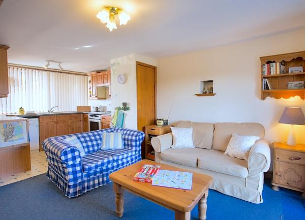 Lounge with 2 sofas and coffee table leading to a fitted kitchen beyond.