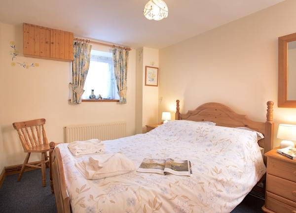 Double bedroom with bed, chest of drawers, mirror and armchair.