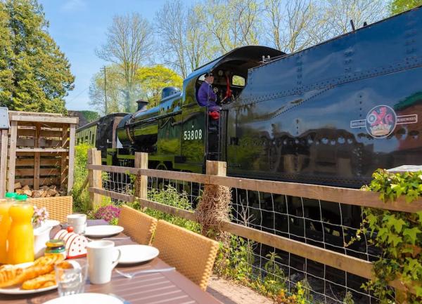 A steam engine powers along tracks opposite a terrace with a table laid for lunch.
