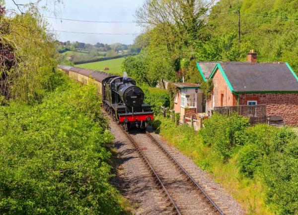 A steam train glides past a railway cottage in the West Somerset countryside.