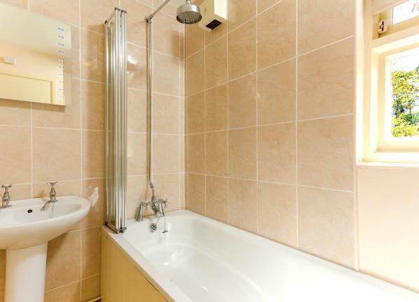 A bathroom with a bath having an overhead shower and wash basin.