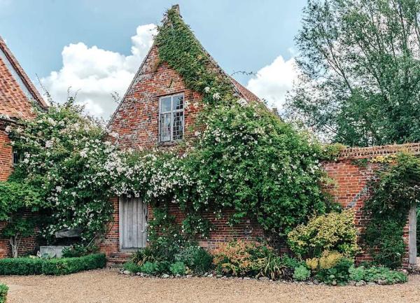 Exterior of an ivy-clad 2 storey Norfolk brick cottage overlooking a courtyard.