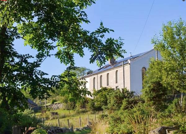 A single storey barn conversion glimpsed through a break in trees.