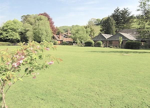 A cluster of sslate-roofed cottages half hidden by trees overlook a large playing field.