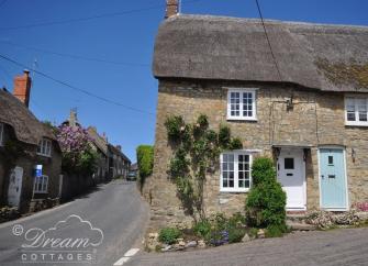 Exterior of a stone-built thatched cottage in Dorset.