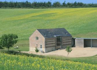 A stone barn stands alone surrounded by wheat fields.