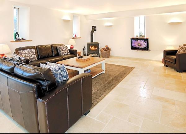 A spacious tiled lounge with two sofas, armchair, wood burner and TV.