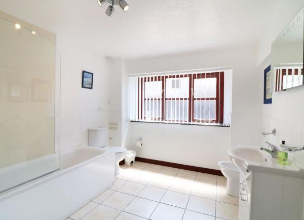 A bathroom with a bath having an overhead shower, WC and washbasin.