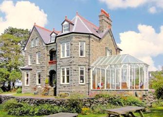 £-storey Stone house and conservatory surrounded by gardens.